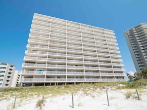 A multi-story hotel with balconies, located near a sandy beach.