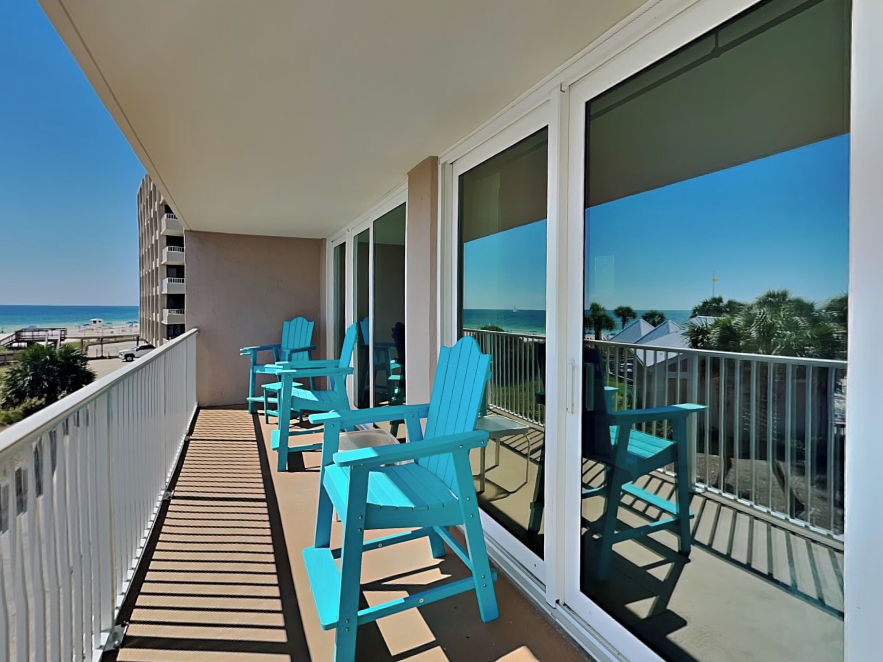 A balcony with blue chairs and a view of the beach.