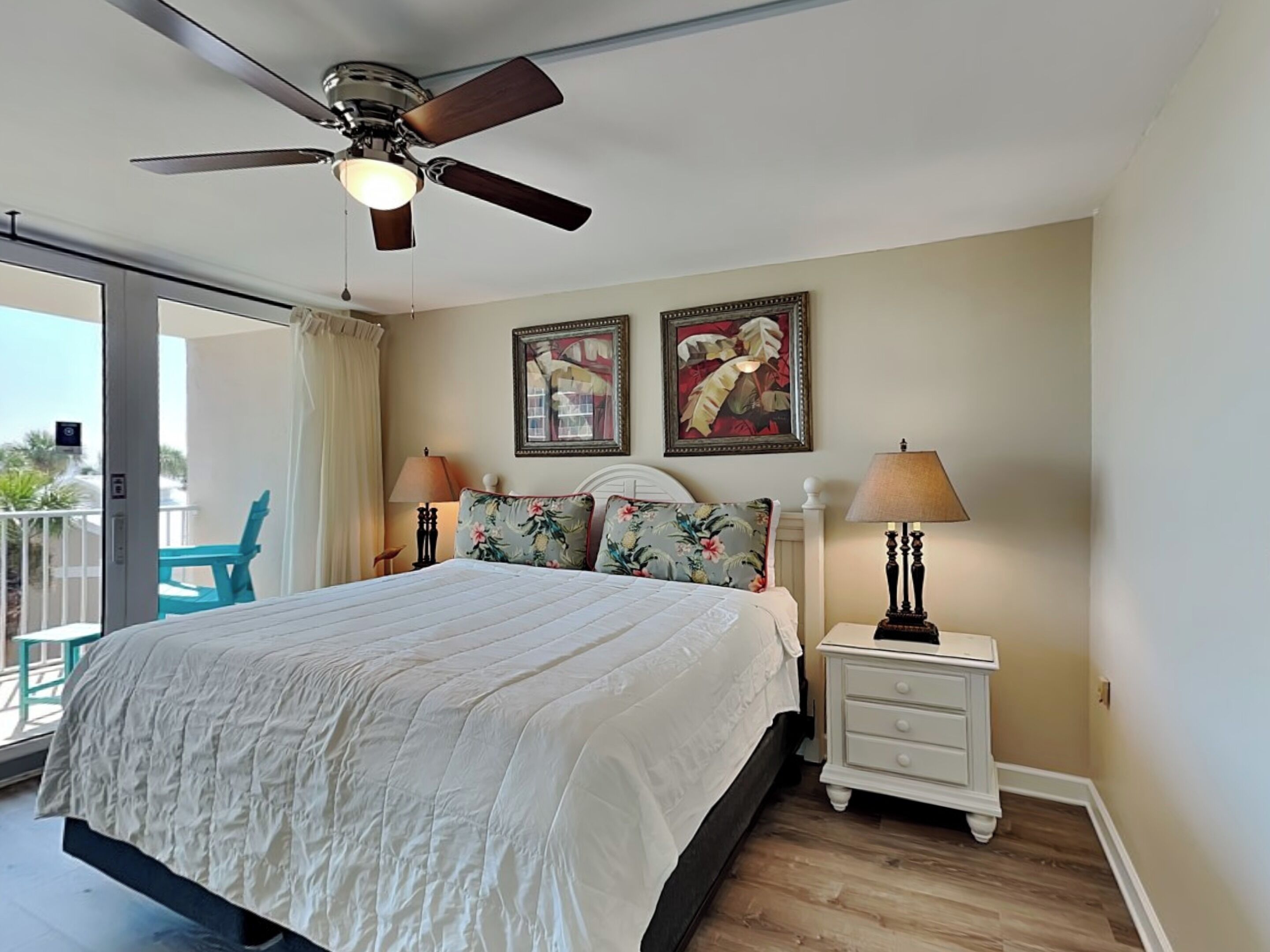 A bedroom with a bed, two nightstands, a ceiling fan, and two wall-mounted paintings.