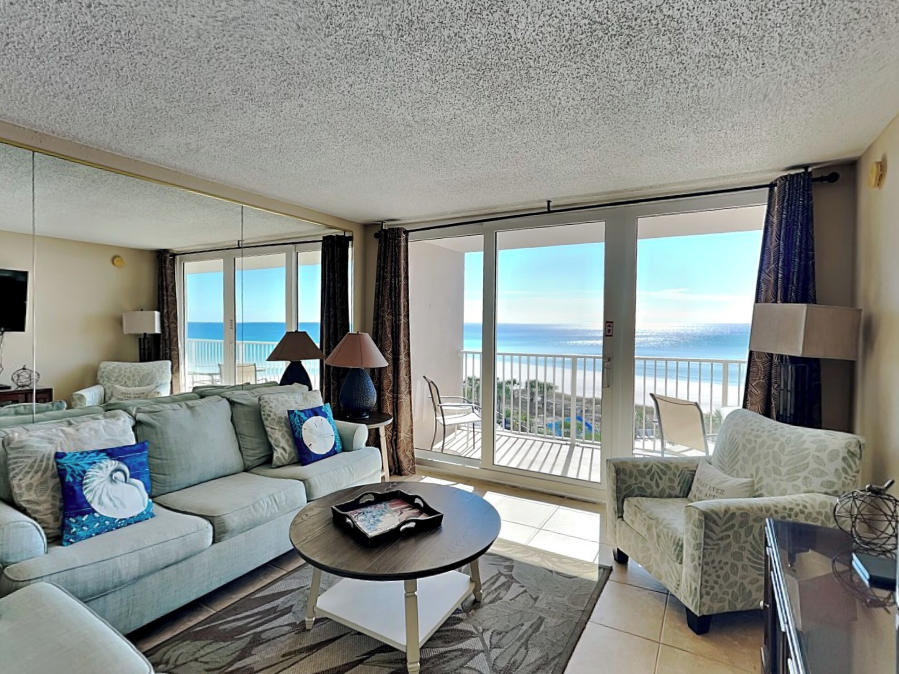 Ein geräumiges Wohnzimmer mit einem Balkon, der auf das Meer blickt, inklusive einer Couch, einem Couchtisch und einem gemusterten Sessel.