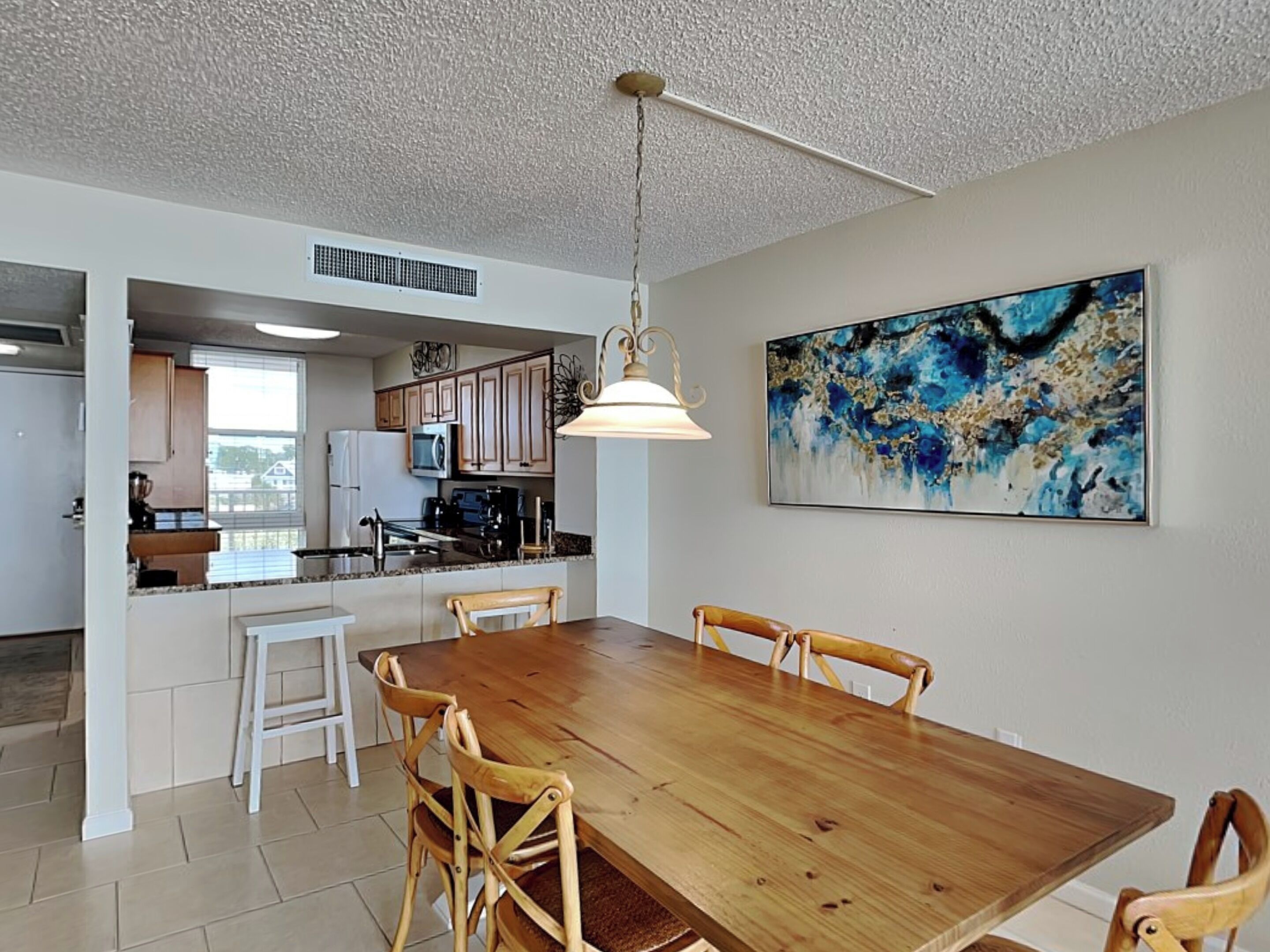 Un comedor amplio con una mesa y sillas de madera, una lámpara colgante y un cuadro abstracto grande en la pared.
