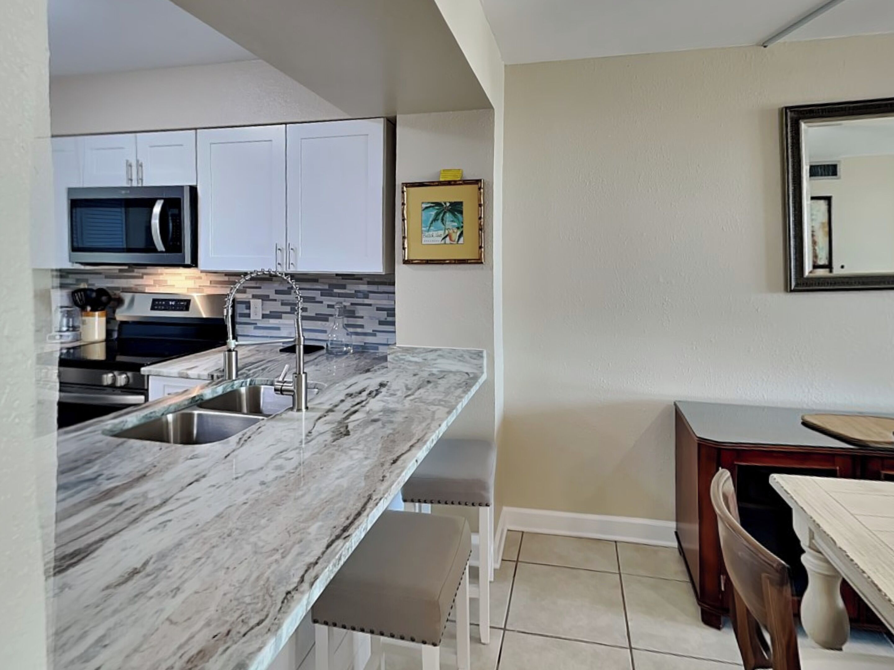 A modern kitchen with white cabinets, a marble countertop, stainless steel appliances, and a tiled backsplash.
