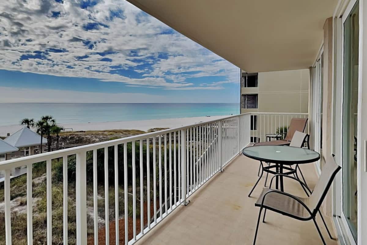 Un balcone con vista sulla spiaggia, un tavolo con sedie e una ringhiera.