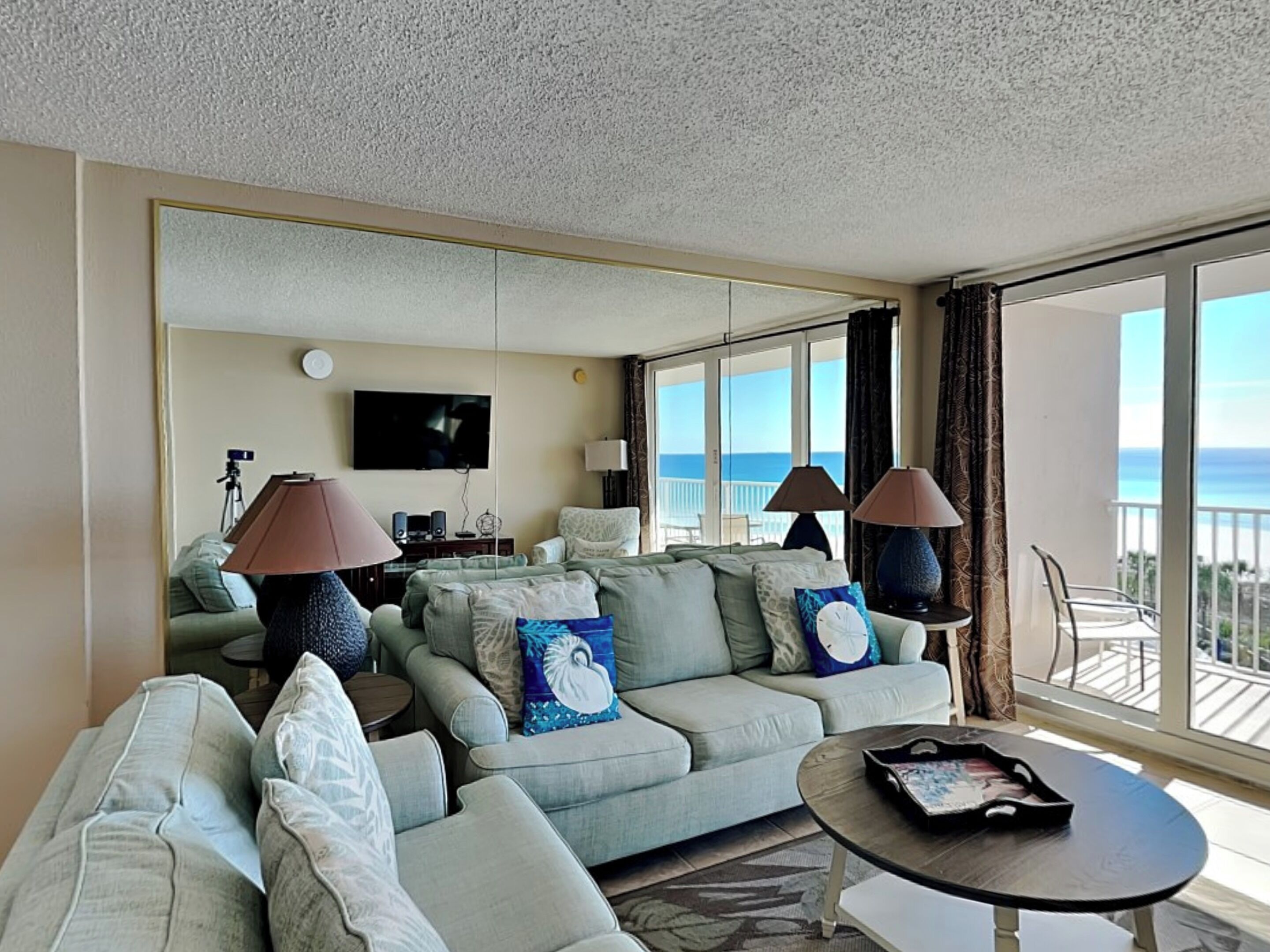 A hotel room with a sofa, armchairs, a coffee table, a TV, and a balcony with a view of the ocean.