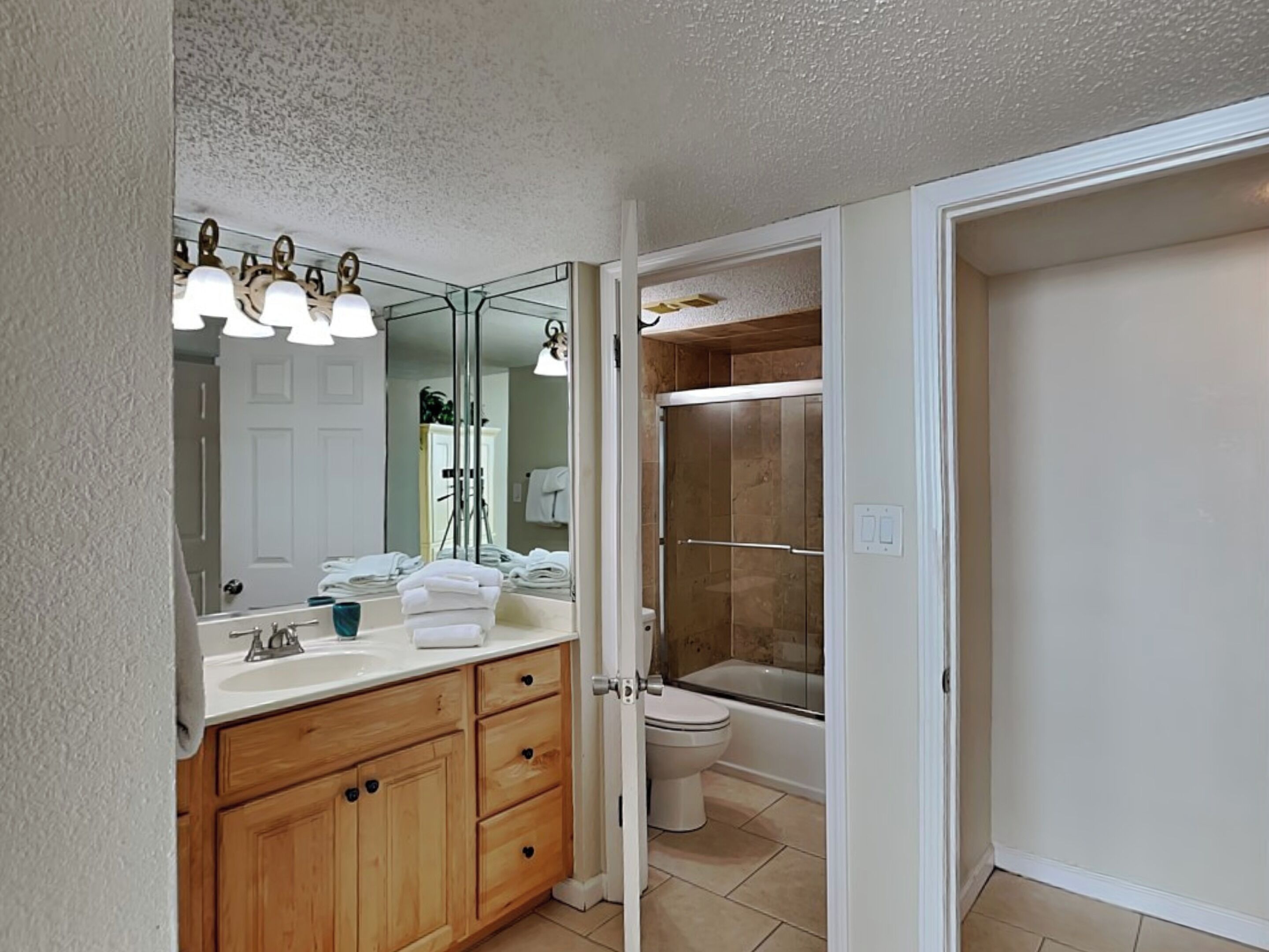 Une salle de bain avec un meuble-lavabo en bois, un grand miroir, des toilettes et un espace douche.