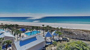 A beach resort with a swimming pool, beach umbrellas, and lounge chairs.
