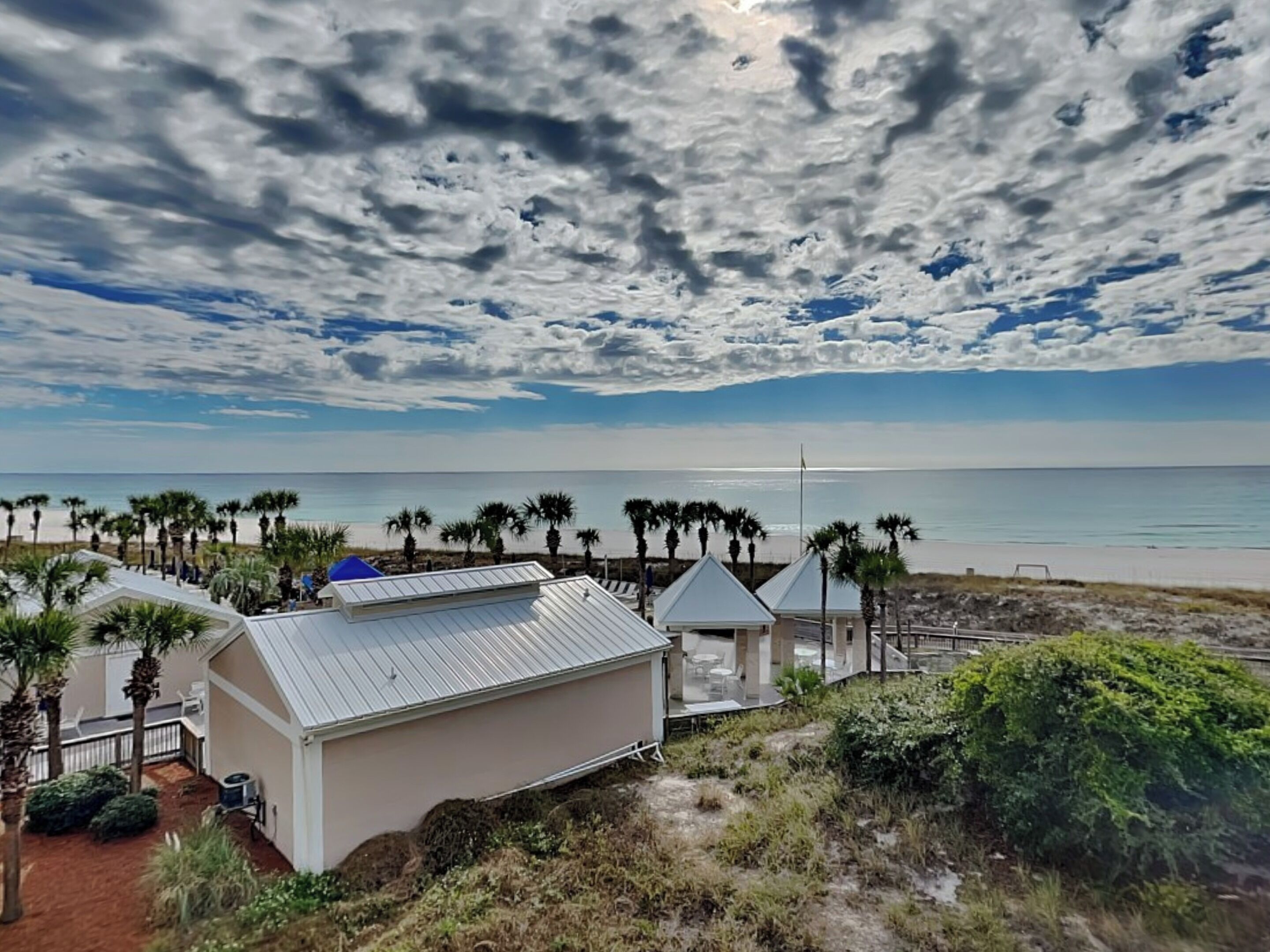 Ein Anwesen am Strand mit einem weißen Gebäude, Palmen und Blick auf den Ozean.