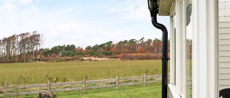 A view from a window overlooking a grassy field with a wooden fence and trees in the background.