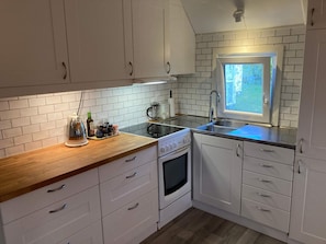 A compact kitchen with white cabinets, a wooden countertop, a built-in oven, and a window with a view of greenery. - 5 Person Holiday Home in Falkenberg (Falkenberg)