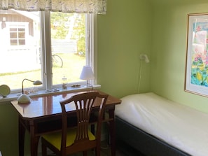 A room with a bed, a desk with a chair, a window with a view of the outside, and a framed picture on the wall. - 5 Person Holiday Home in Falkenberg (Falkenberg)