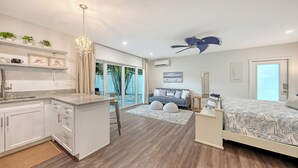 A modern kitchen with a central island, a dining area with a view, a bedroom with a bed and a nightstand, and a living area with a sofa and a coffee table. - 2 Primary Suites | FREE Pool Heat | Great Beaches (Sarasota)