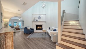 A spacious living room with a fireplace, a staircase, and a view of the kitchen. - 2 Primary Suites | FREE Pool Heat | Great Beaches (Sarasota)