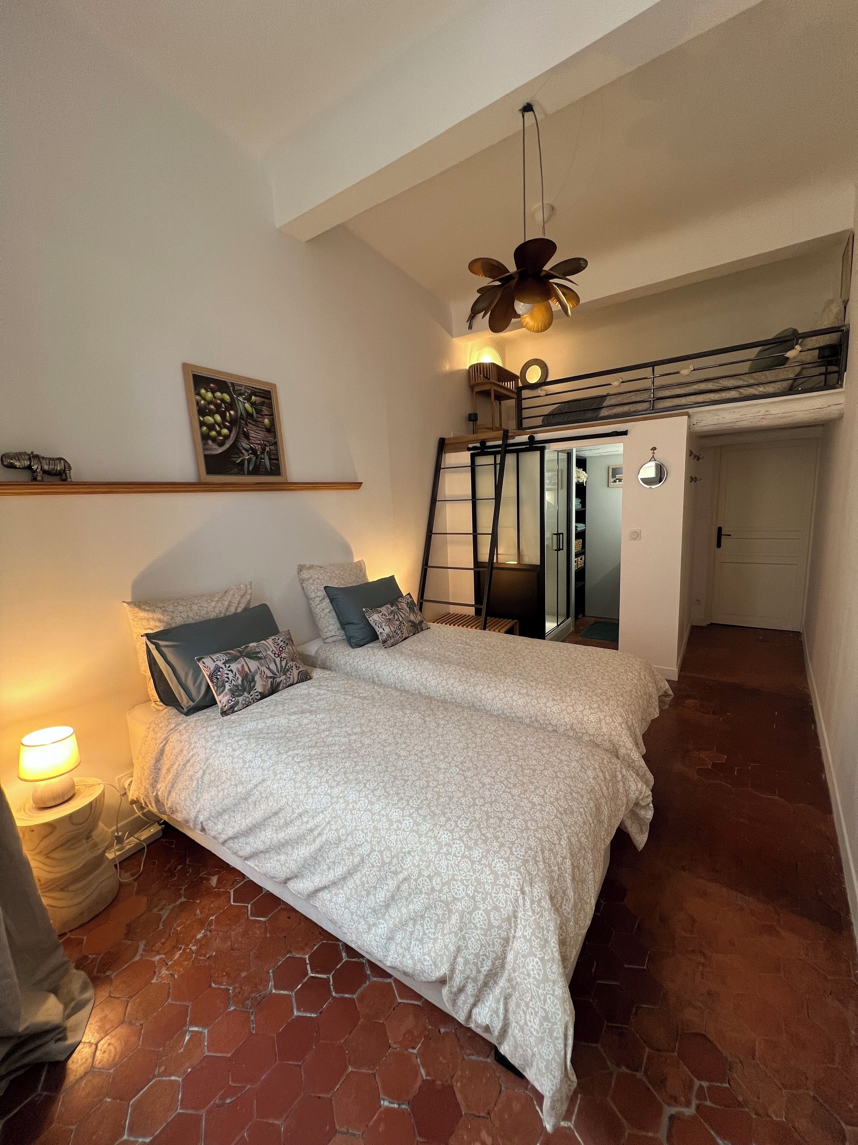 A bedroom with a bed, a nightstand, a lamp, a ceiling fan, a loft bed, and a door.