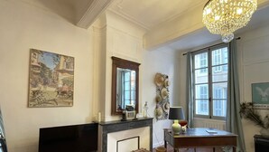 Een woonkamer met een open haard, een televisie, een kroonluchter en een raam met luiken.