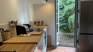 Een moderne keuken met een houten aanrecht, een roestvrijstalen koelkast, en uitzicht op groen via een geopende deur.