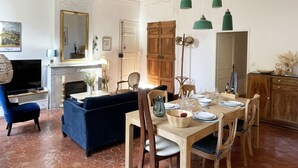 Een eetgedeelte met een houten tafel gedekt voor vier personen, een blauwe bank en een open haard.