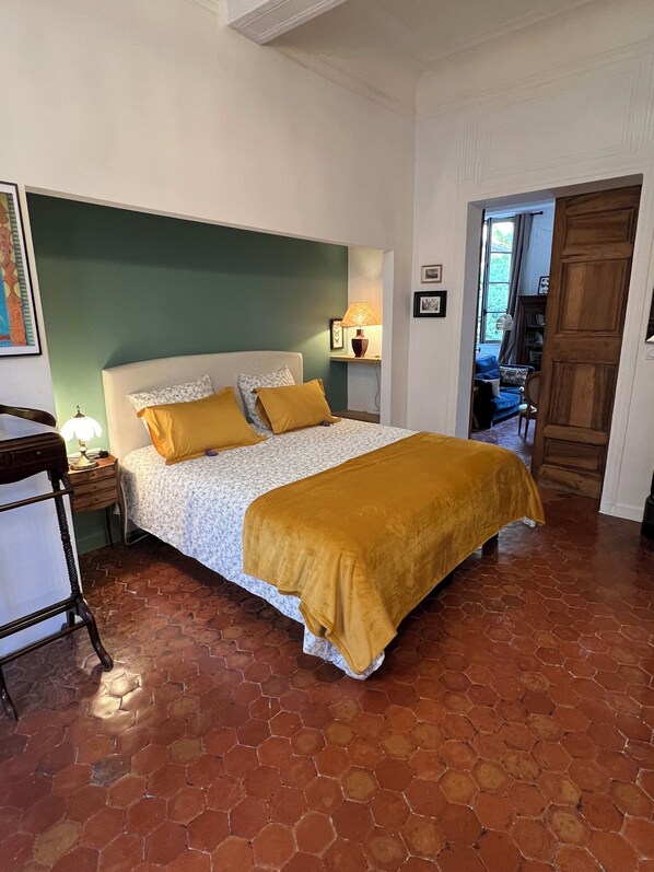 Une chambre à coucher avec un lit, une table de chevet, une lampe et une vue sur le salon, grâce à une porte ouverte.