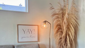 A grey sofa with a framed sign that reads "YAY! you're here." next to a tall potted plant and a floor lamp.