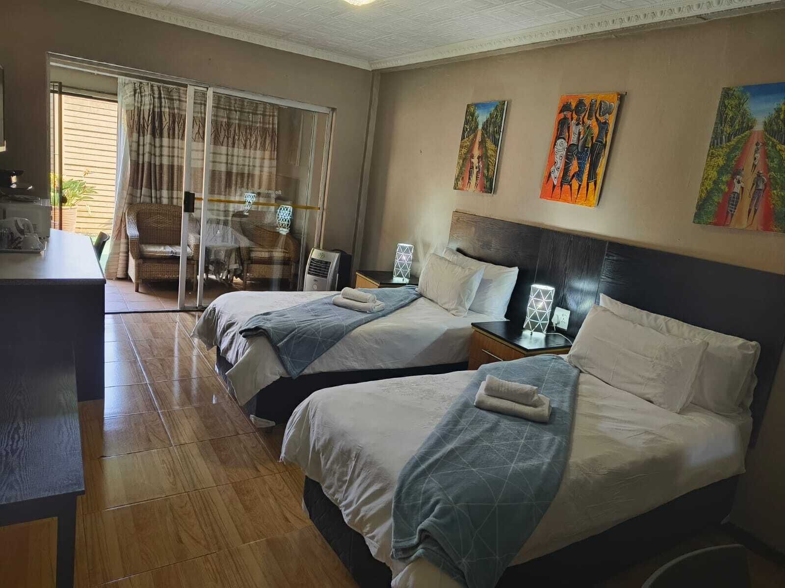 Habitación de hotel con dos camas, un escritorio, una silla y una puerta corrediza de vidrio que da a un balcón.