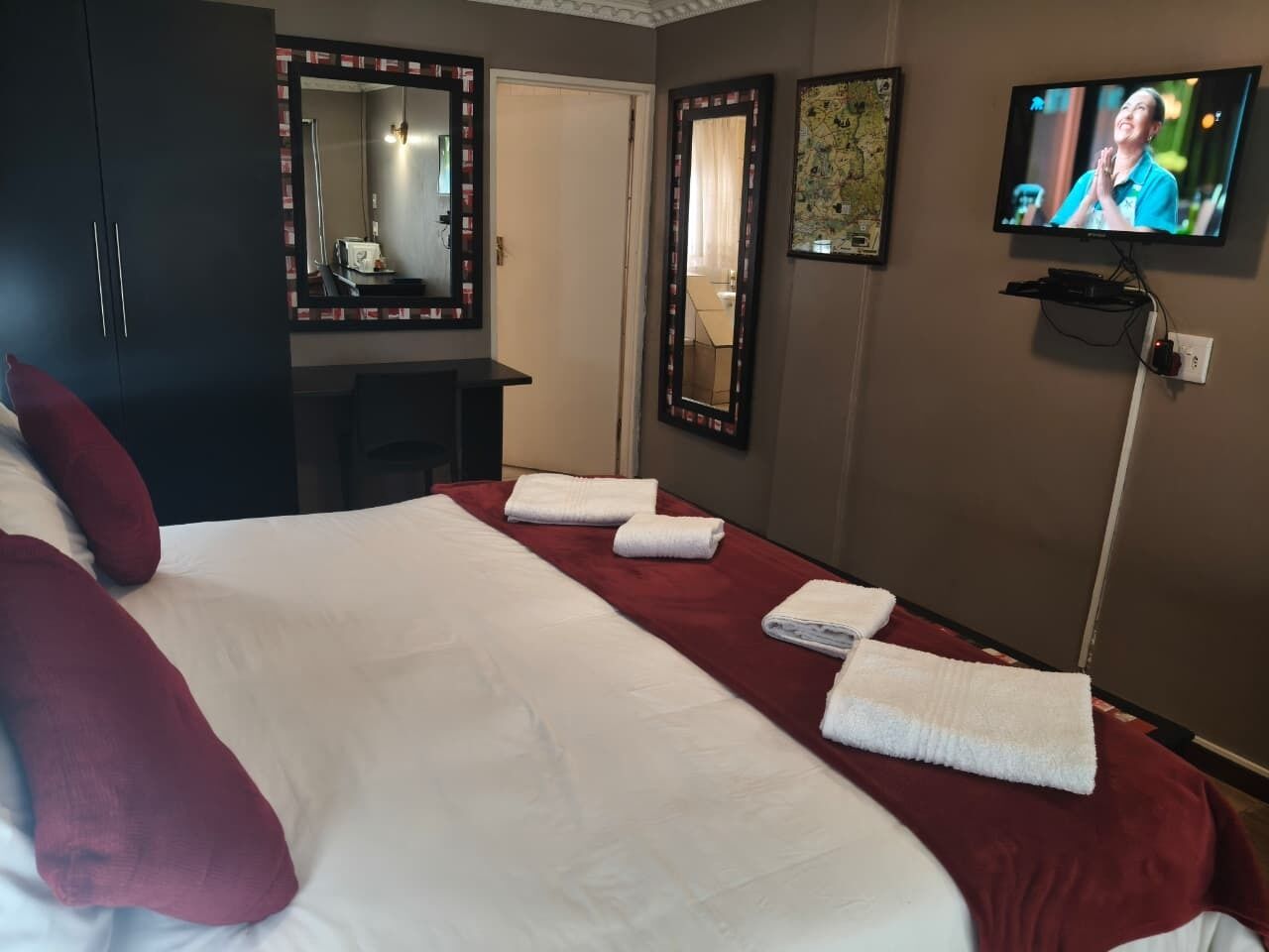 A hotel room with a large bed, a television, and a mirror.