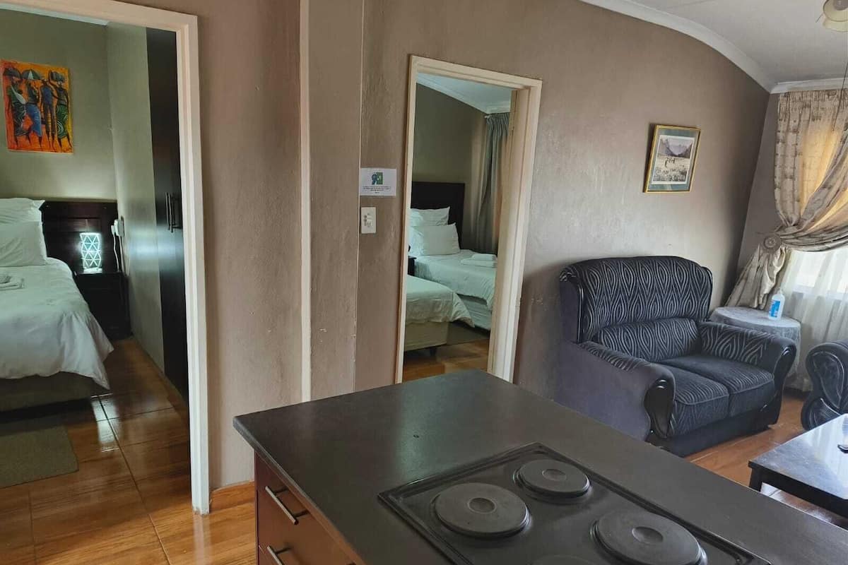 Une chambre d’hôtel compacte comprenant un coin cuisine, un canapé, un lit et un tableau au mur.