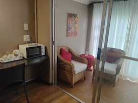 Una habitación con un microondas en la encimera, una silla de mimbre con un cojín rojo, una mesita con una botella y un cuadro en la pared.