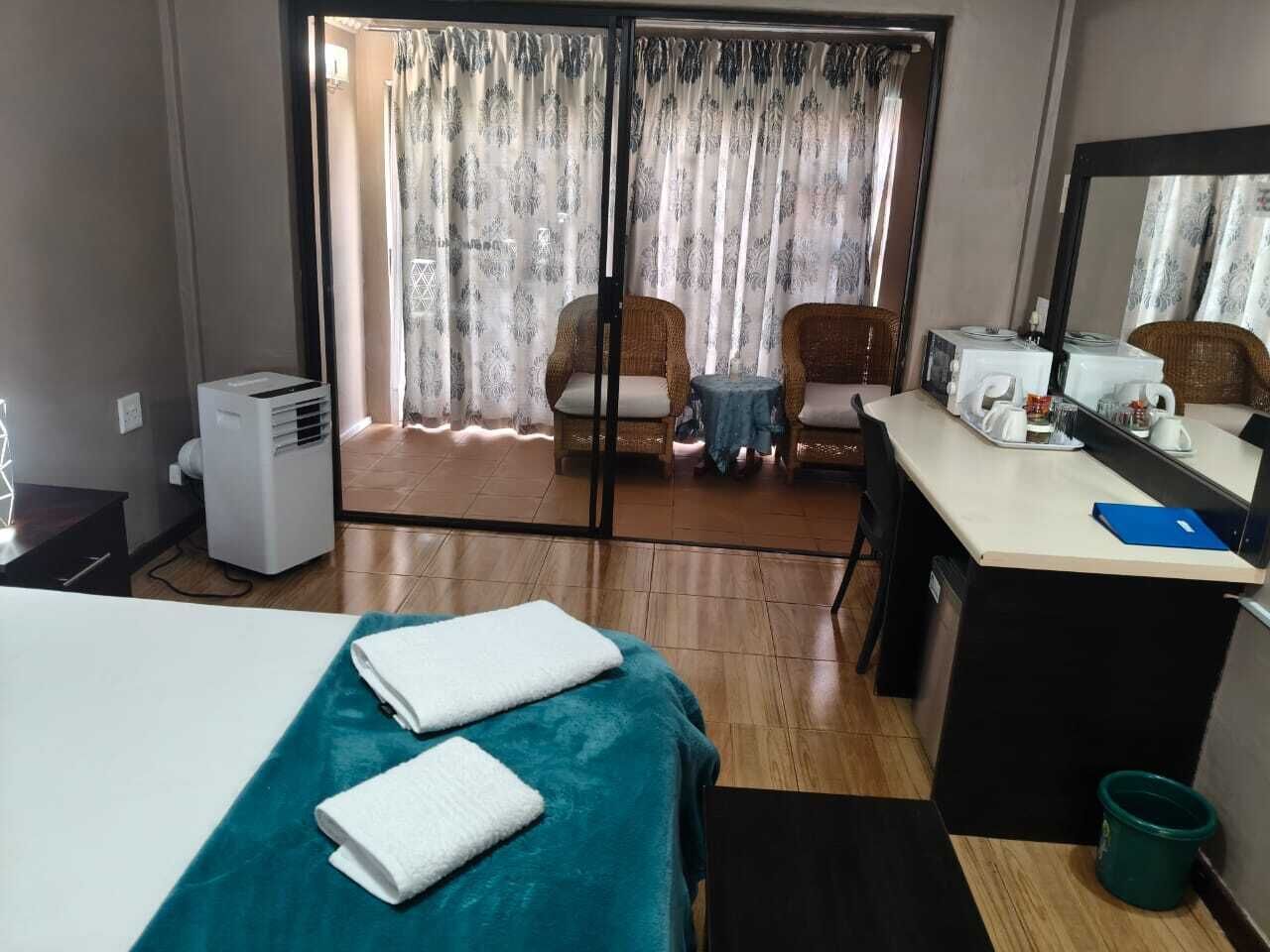 A hotel room with a bed, a desk, a chair, a small table, a microwave, a kettle, and a window with curtains.