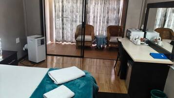 A hotel room with a bed, a desk, a chair, a small table, a microwave, a kettle, and a window with curtains.