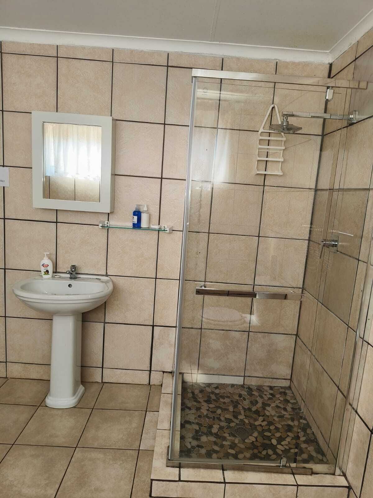 A bathroom with a pedestal sink, a mirror, and a glass-enclosed shower area.