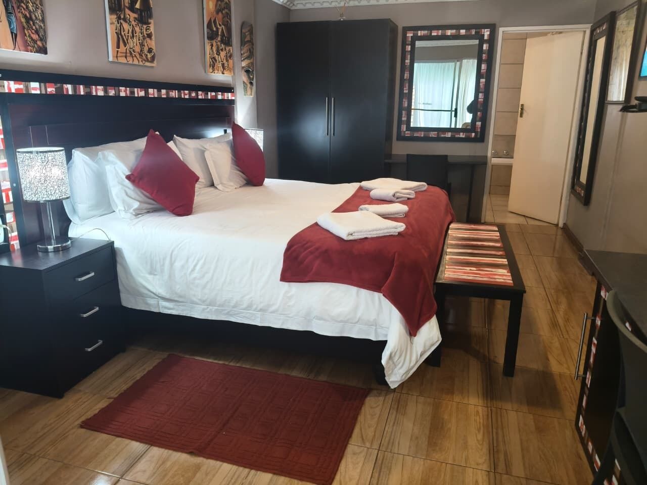 Habitación de hotel con cama, mesita de noche, armario y un espejo, además de una alfombra roja.