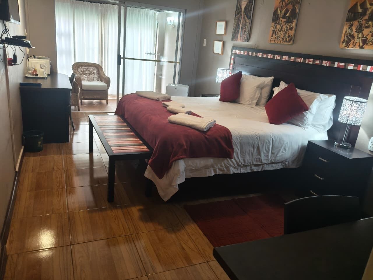 A hotel room with a large bed, a bedside table, a chair, a desk, and a window with curtains.