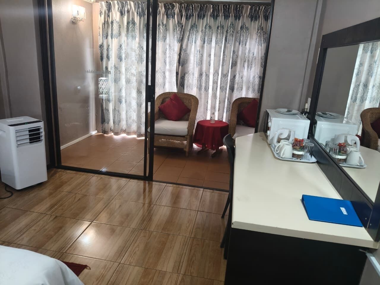 Een hotelkamer met een schuifdeur naar een balkon, een bureau met spiegel en een kleine tafel met een rode tafelkleed.