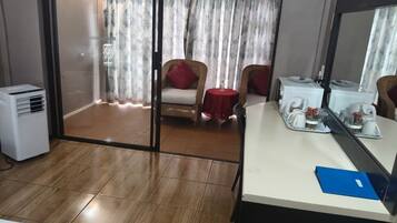 Een hotelkamer met een schuifdeur naar een balkon, een bureau met spiegel en een kleine tafel met een rode tafelkleed.