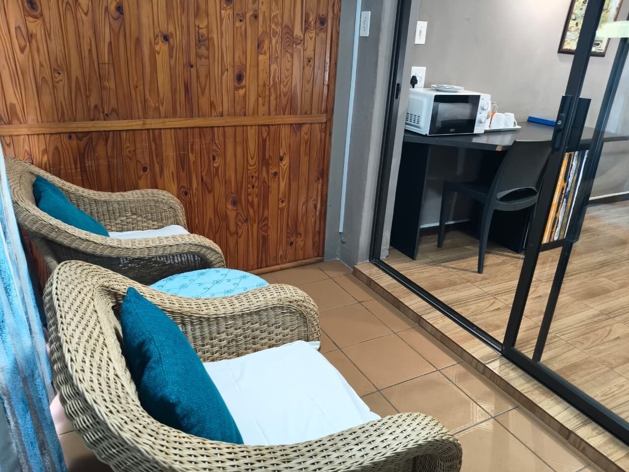 A room with wicker chairs, a wooden wall, a tiled floor, and a table with a microwave.
