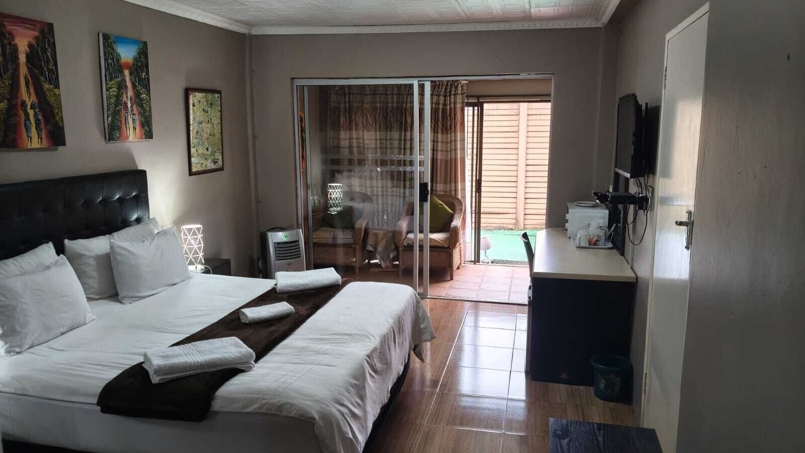 A hotel room with a large bed, a desk, a television, and a sliding glass door leading to an outdoor area.