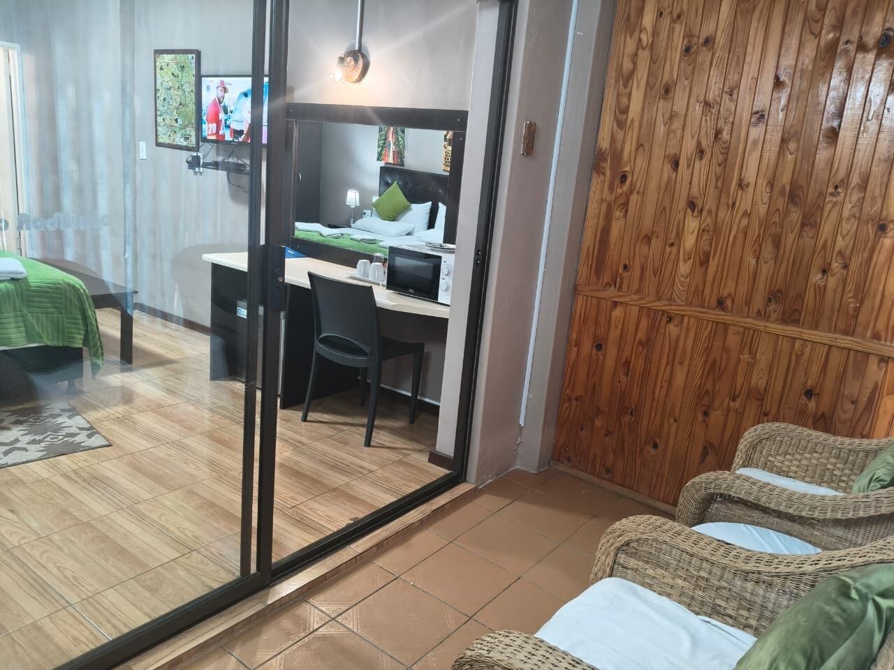 Habitación de hotel con una cama, un escritorio con ordenador, una silla y un sofá de mimbre.