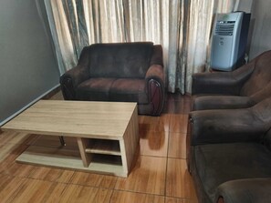 A living room with a wooden coffee table, two brown leather sofas, and a standing heater. - Blyde lodge (Graskop)