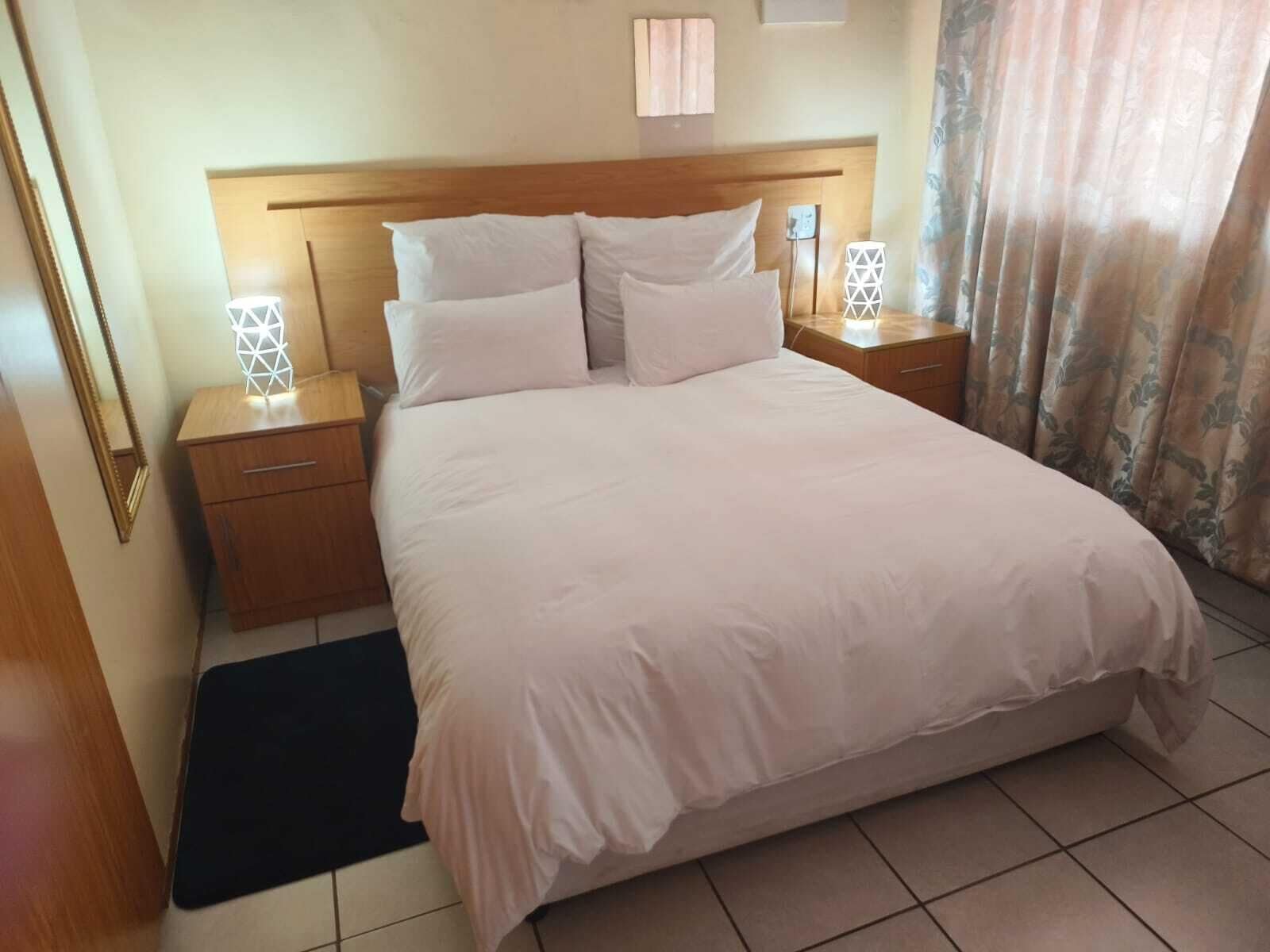 A neatly made bed with white linens, two bedside tables with geometric lamps, a wooden headboard, and a dark rug on the floor.