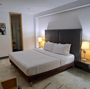 A hotel room with a bed, two bedside lamps, a nightstand, a mirror, and a door. - HOTEL KING VERSALLES (Cali)