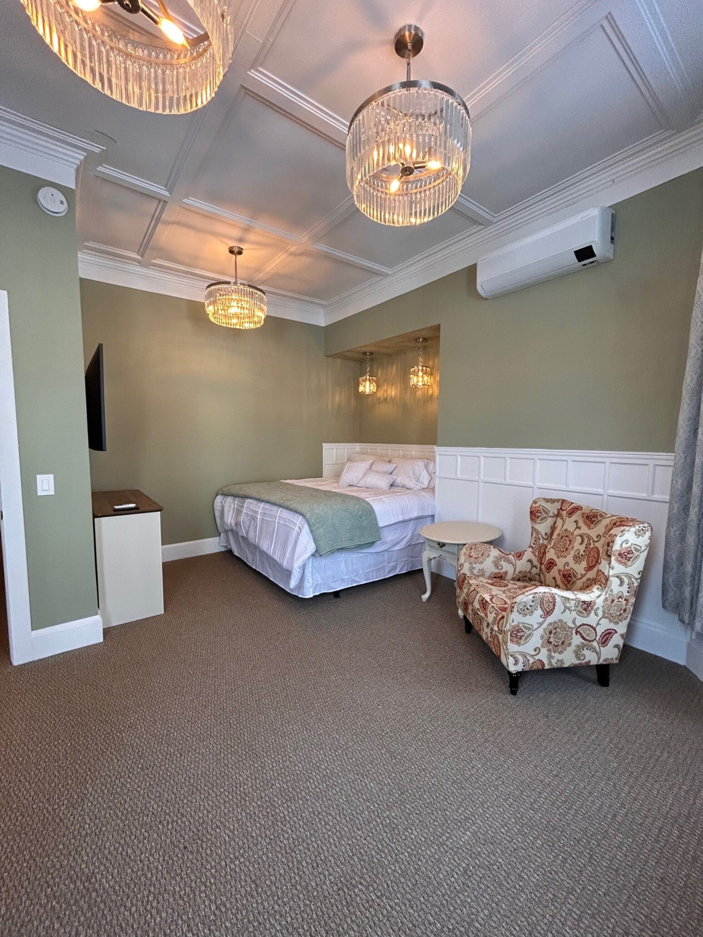 Un dormitorio con cama, una silla, una mesita y dos candelabros.