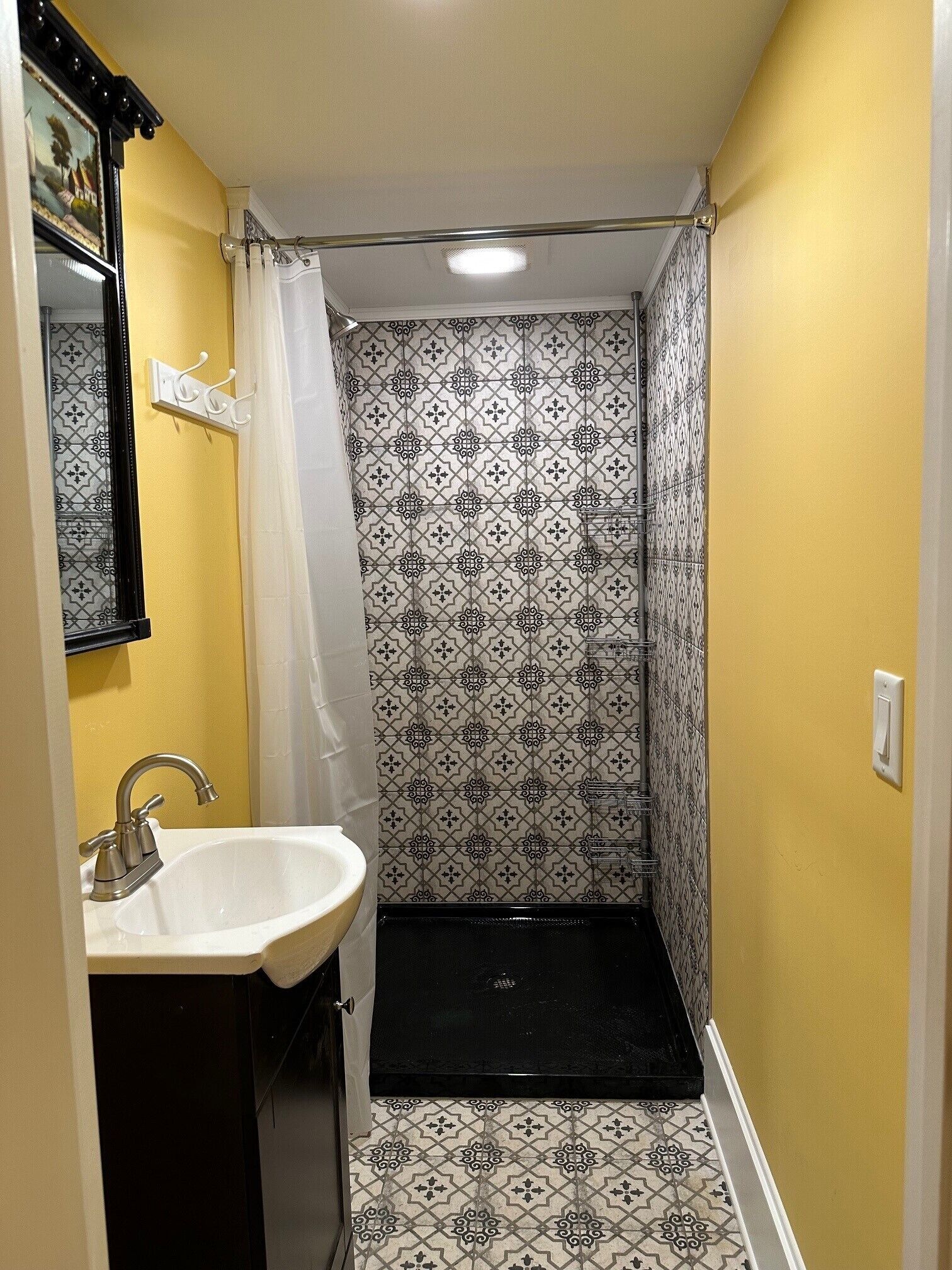 Ein Badezimmer mit einem weißen Waschbecken, einer Dusche mit gemusterten Fliesen und einer gelben Wand.