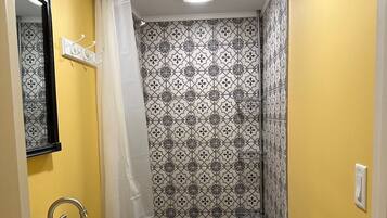 Ein Badezimmer mit einem weißen Waschbecken, einer Dusche mit gemusterten Fliesen und einer gelben Wand.