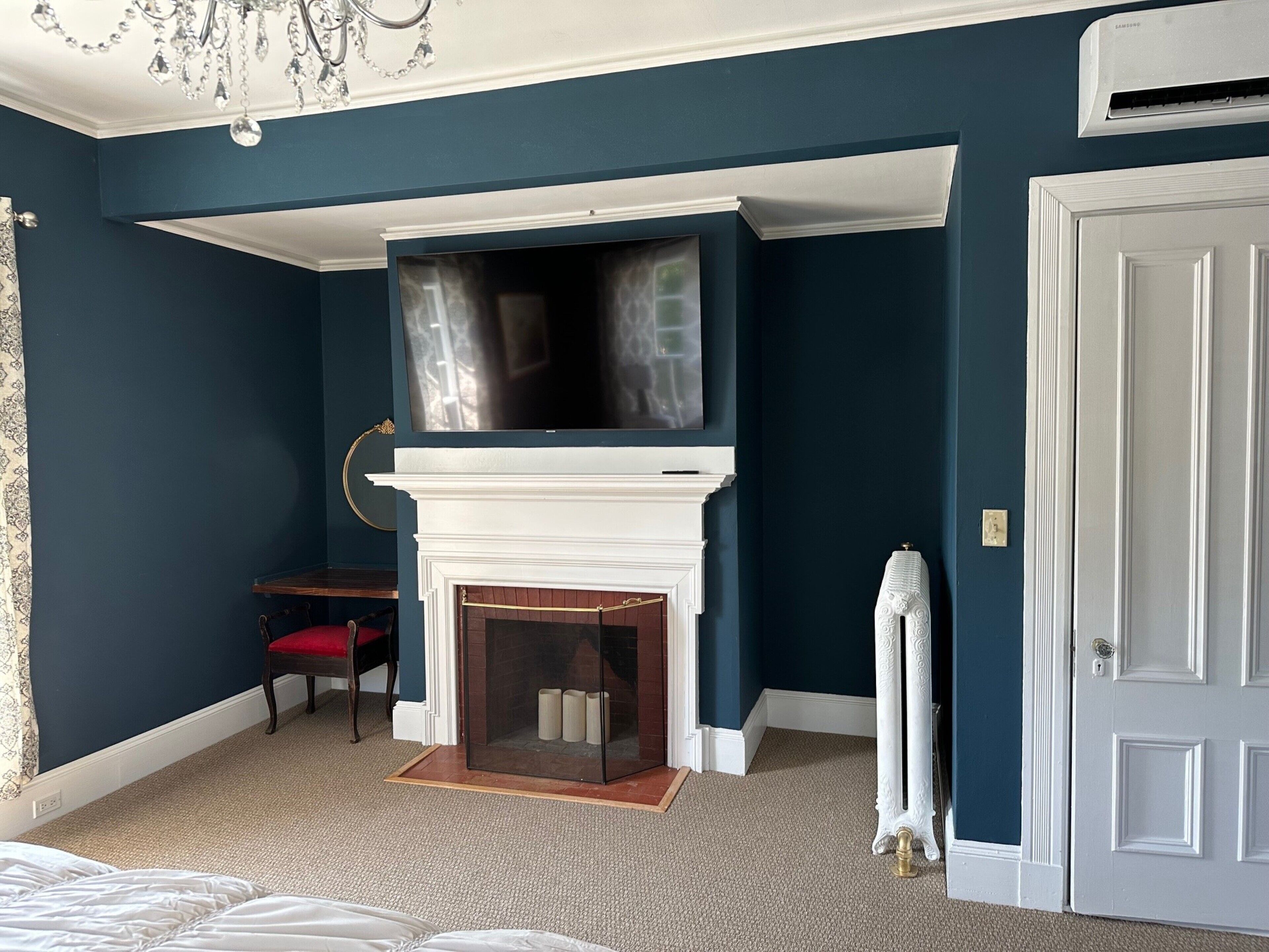 Una habitación con chimenea blanca, televisor montado, sillón rojo y radiador blanco.