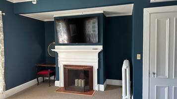 Una habitación con chimenea blanca, televisor montado, sillón rojo y radiador blanco.