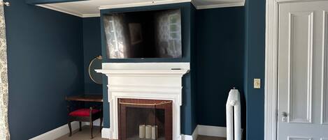 A room with a white fireplace, a mounted TV, a red chair, and a white radiator.