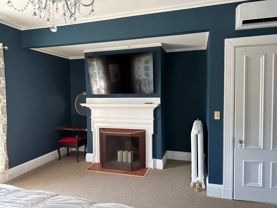Una habitación con chimenea blanca, televisor montado, sillón rojo y radiador blanco.