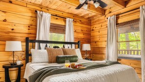 A wooden cabin bedroom with a bed, two bedside tables, and a window with curtains.