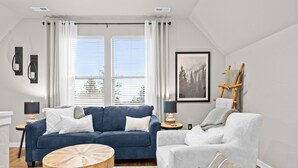 Un salón moderno con un sofá azul, un sillón blanco, una mesa de centro redonda de madera y un cuadro en la pared.