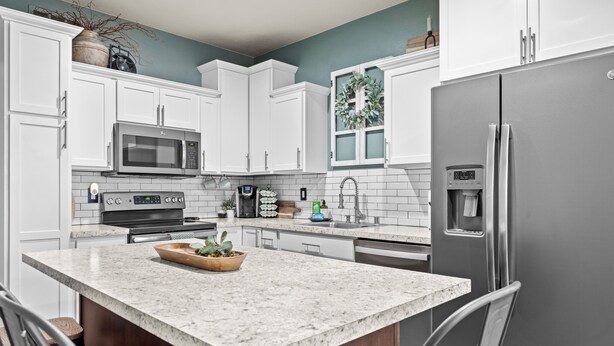 Una cocina moderna con armarios blancos, un refrigerador de acero inoxidable, una encimera de granito y una isla integrada con asientos.