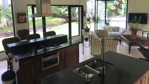 Cozinha moderna com ilha central, área de refeições com cadeiras, sofá e televisão.